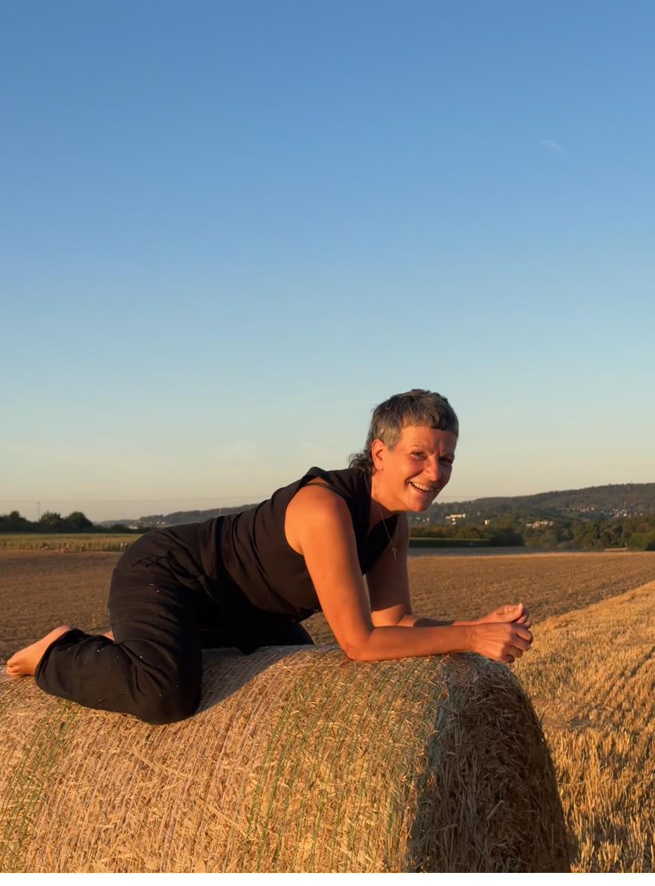 Vera liegt entspannt auf einem Heuballen und lächelt in der goldenen Abendsonne.