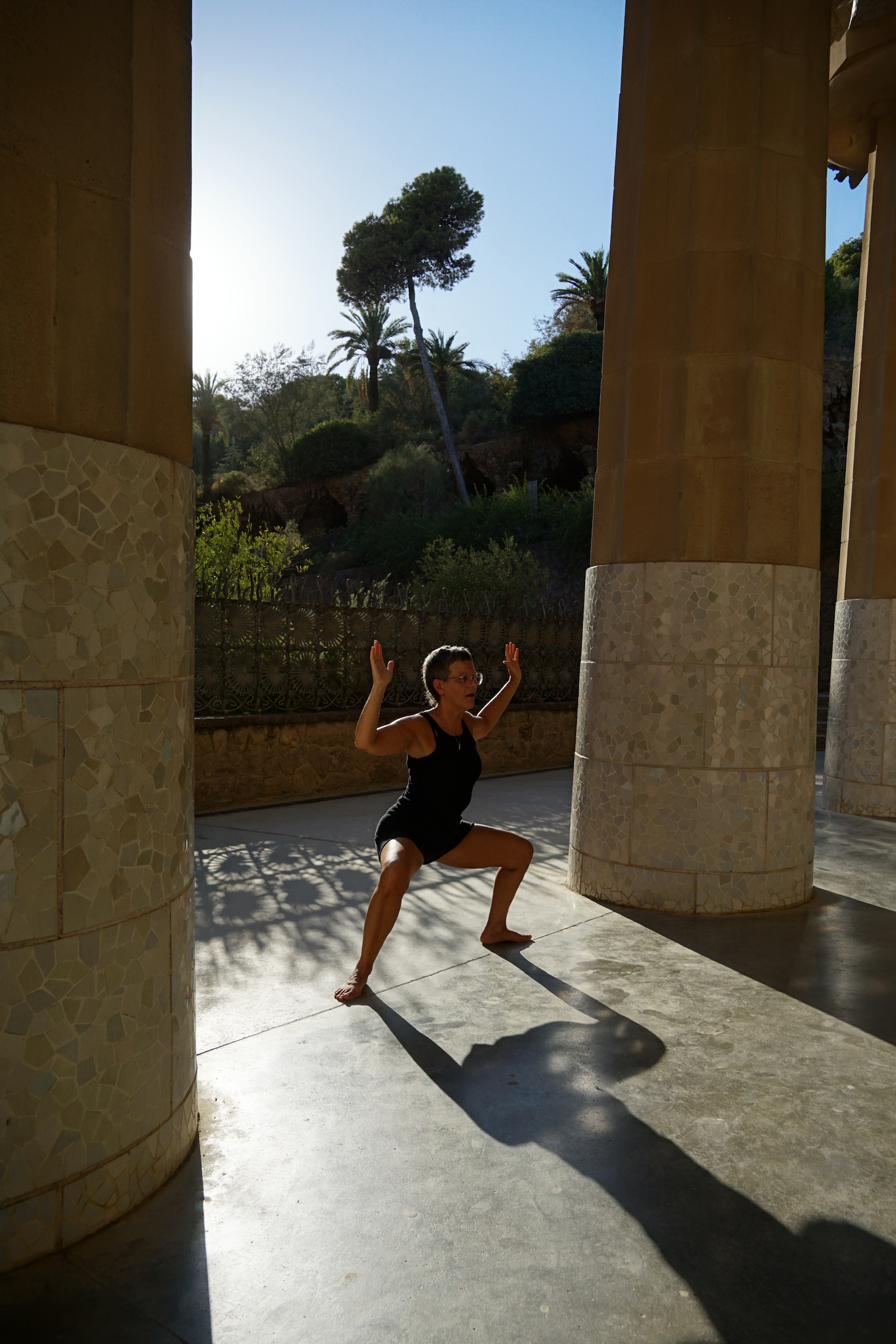 Vera macht Yoga zwischen steinernen Säulen. Lange Schatten fallen auf den Boden.