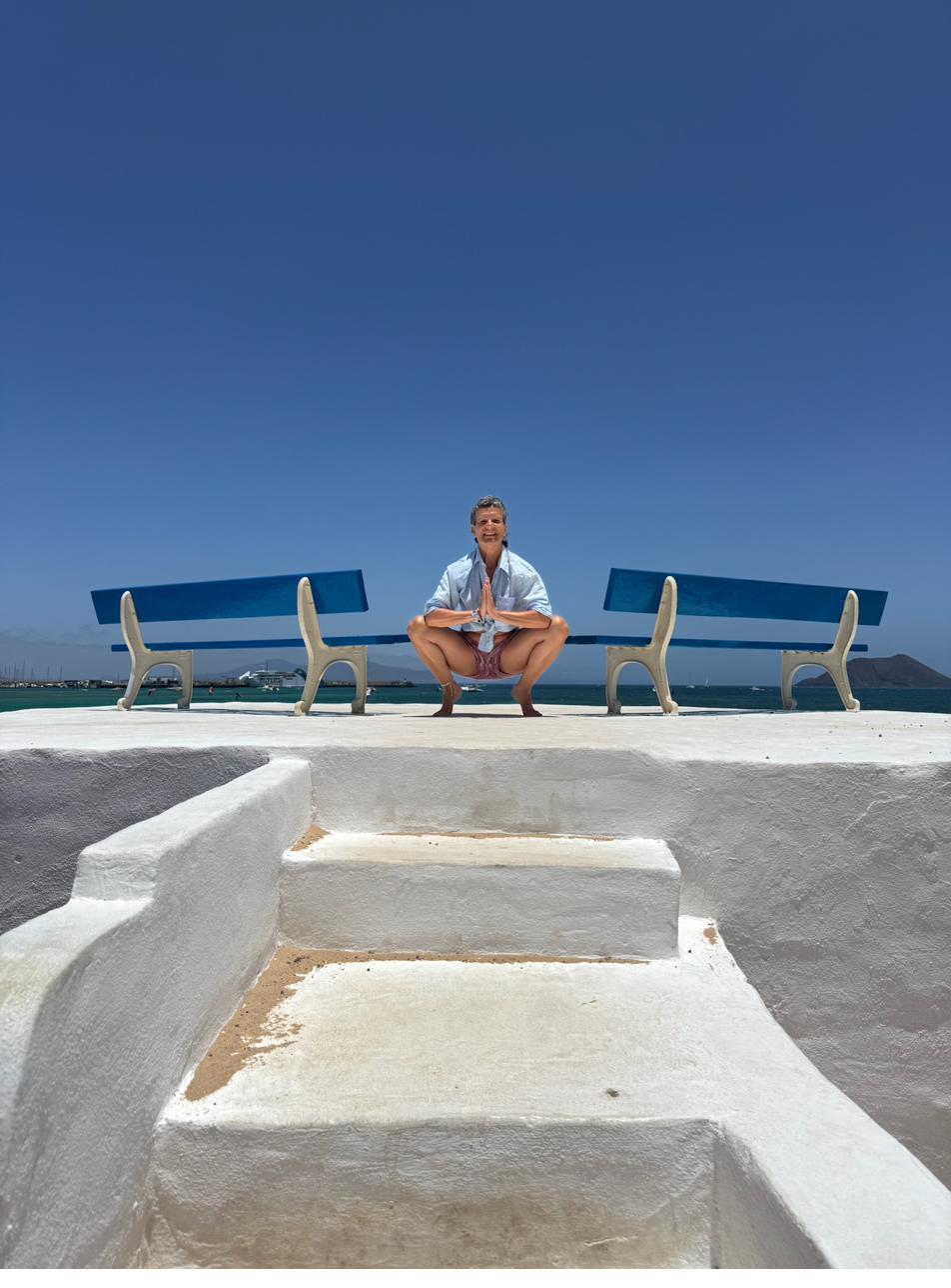 Vera macht Yoga auf einer weißen Terrasse vor dem tiefblauen Meer.